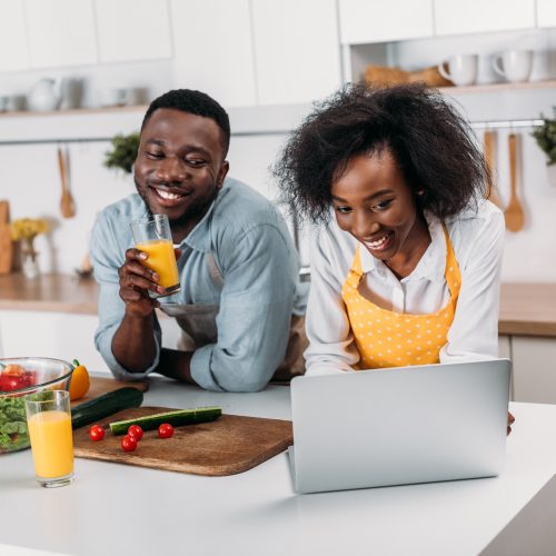African american couple having fun with laptop in kitchen
