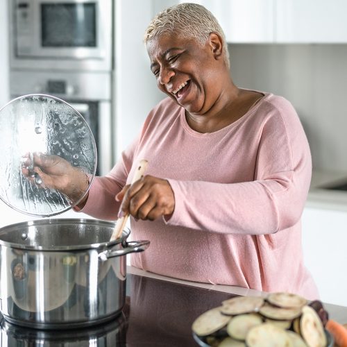 Happy senior woman having fun preparing lunch in modern kitchen - Hispanic Mother cooking for the family at home